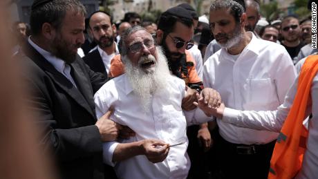 Des juifs ultra-orthodoxes en deuil encerclent un homme accablé de chagrin après l’attaque.