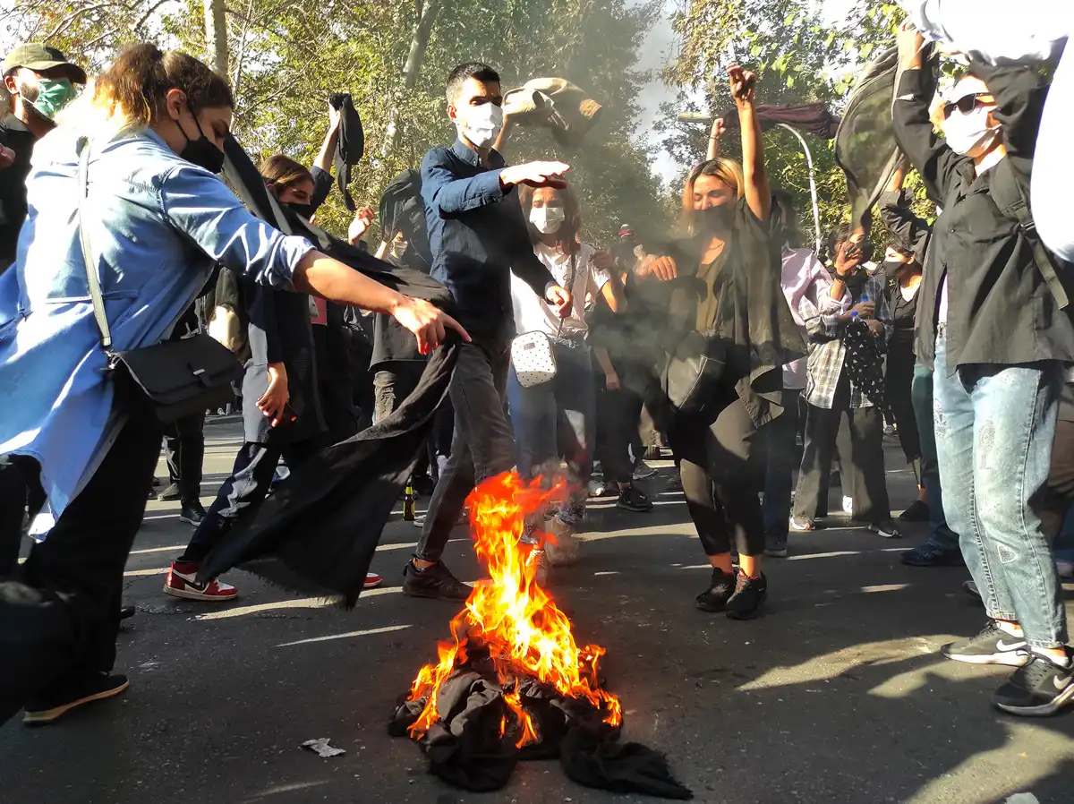 Un groupe de jeunes portant des masques médicaux sautent les poings en l’air autour d’un tas de matériaux noirs qui a été incendié.